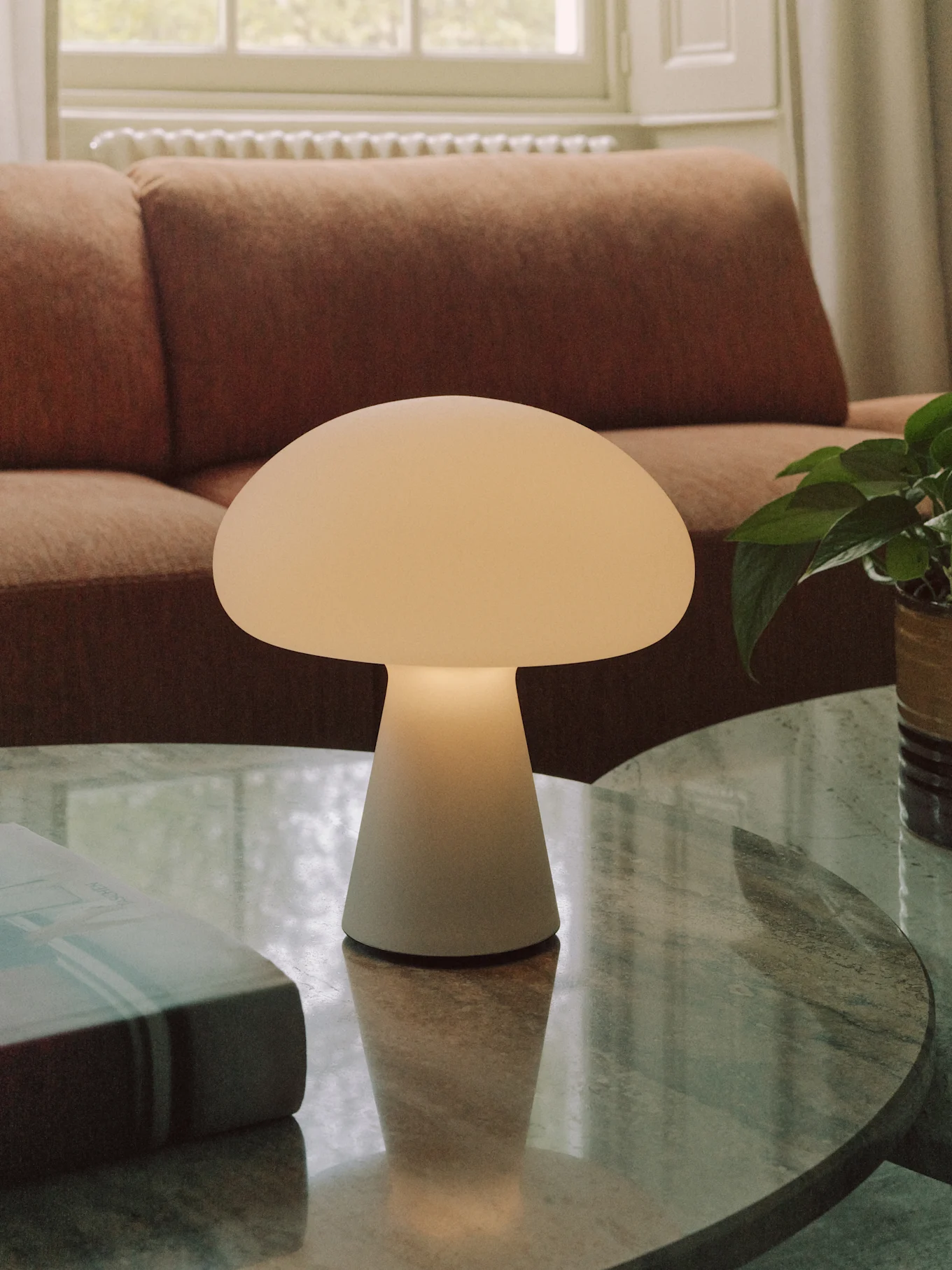 En hvid, champignonformet bordlampe står på et rundt sofabord i marmor i en stue.