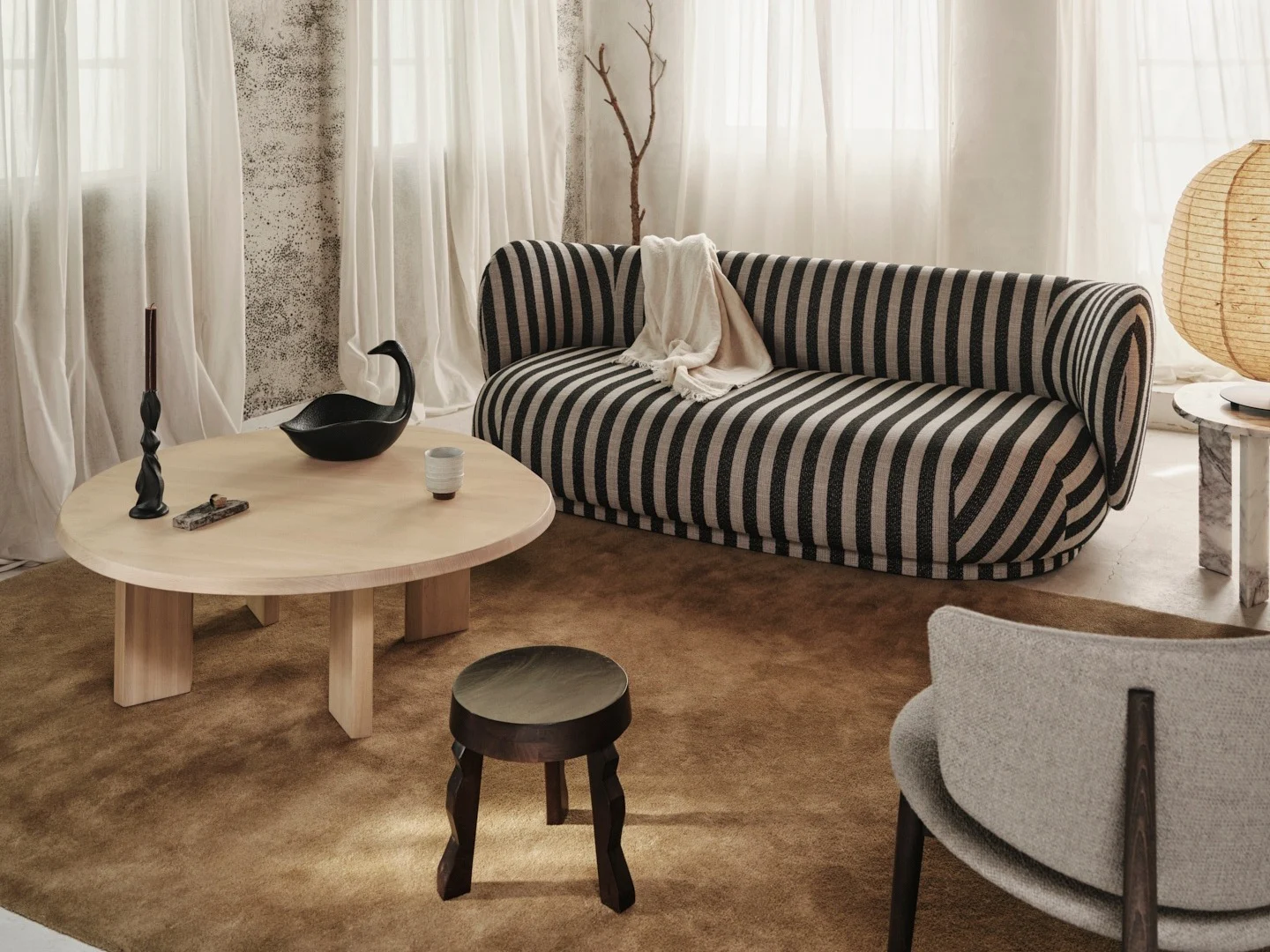 Hyggelig stue med en sort og råhvid stribet sofa, lyst træ sofabord og rustikt bjælkeloft.