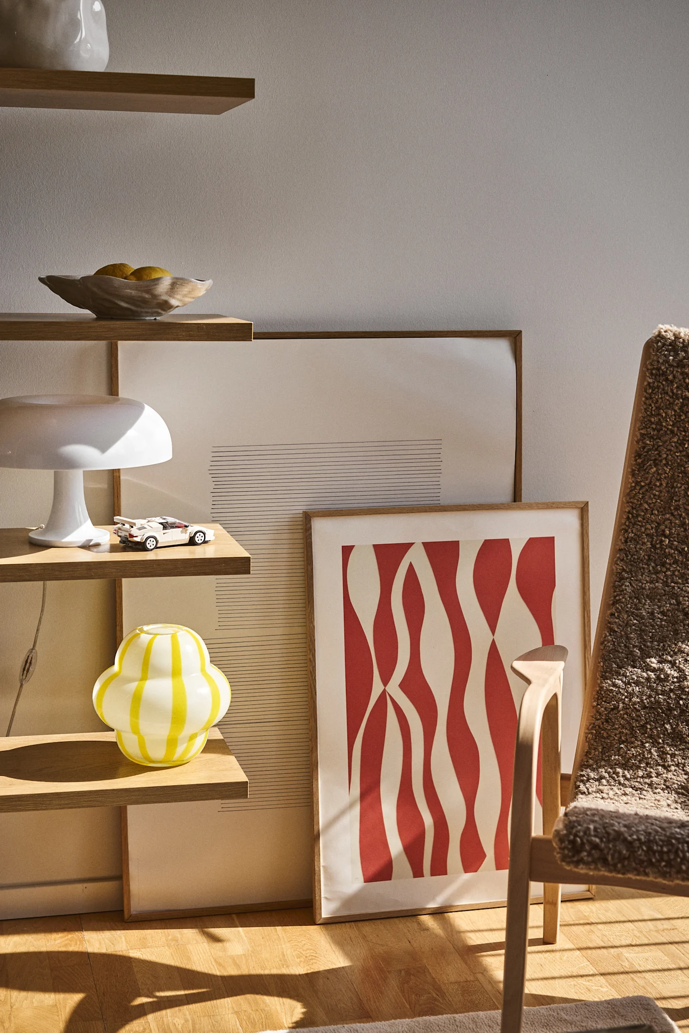 Curlie vasen fra Byon har et rundt, bobblet design i gule og hvide striber. Her placeret i en åben boghylde sammen med Shell skålen, lamper og rammer.