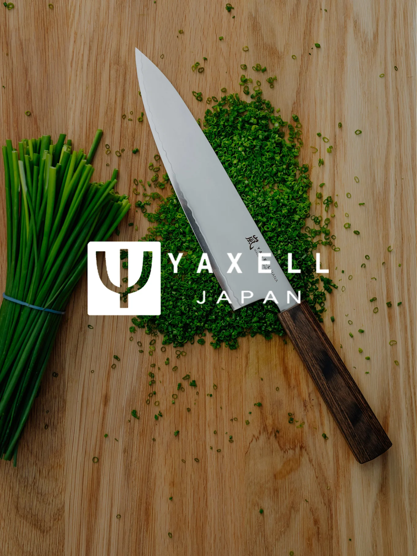 Yaxell kokkekniv, hakkede purløg og et bundt purløg på et træskærebræt med Yaxell Japan-logo.