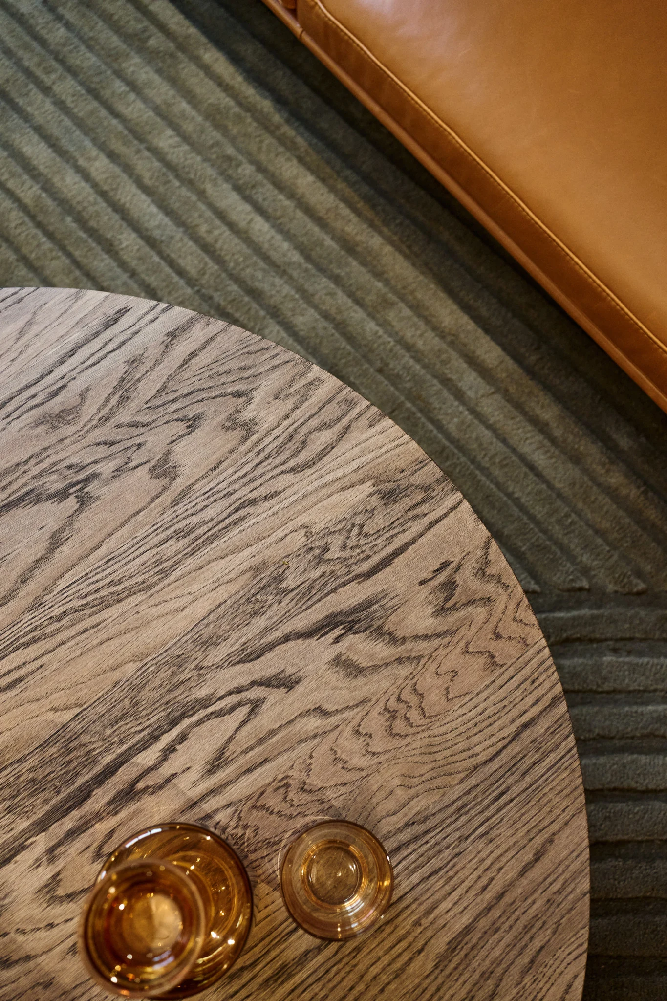 Et sofabord med en mørkebrun bordplade står foran en sofa med forskellige ravfarvede glas fra Raise-kollektionen fra Muuto ovenpå.