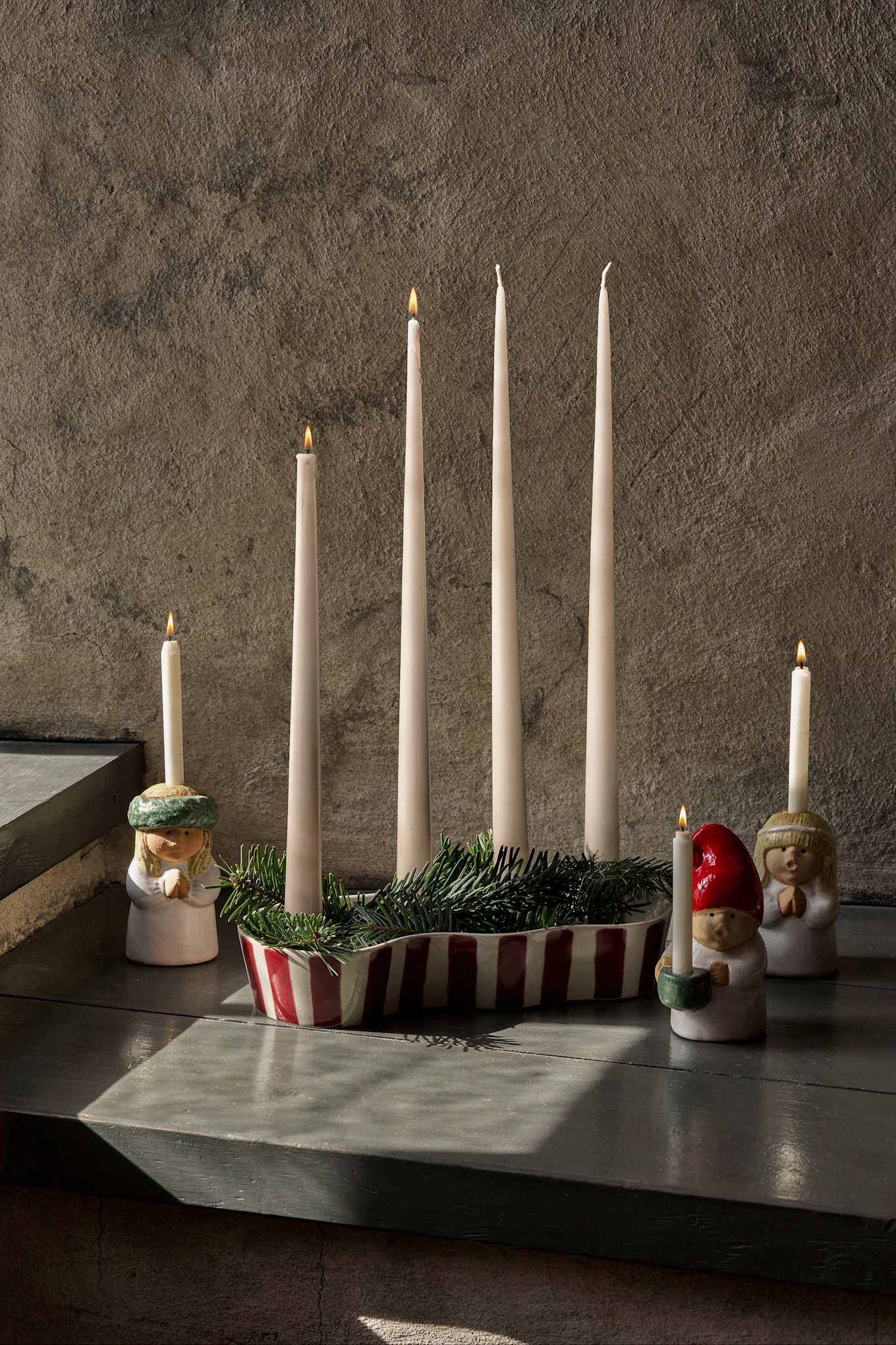 Adventsdekoration med fire uantændte hvide lys, grankviste og tre figurer med tændte lys.