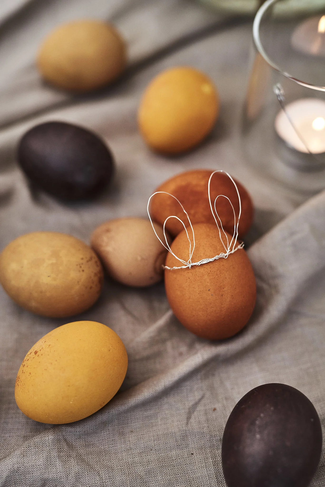 Flere naturligt farvede æg, hvoraf det ene har kaninører af tråd.