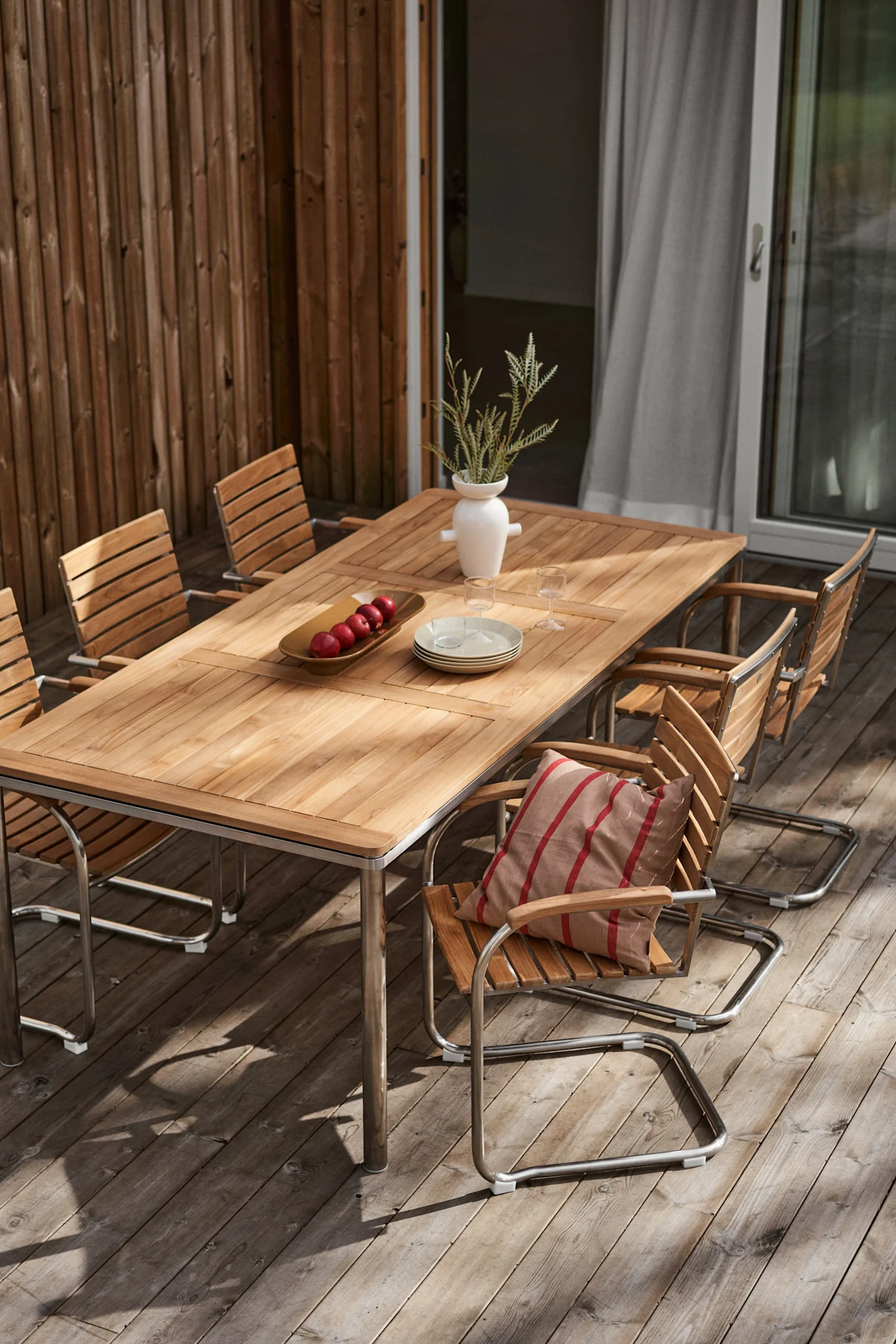 En terrasse med en hyggelig spiseplads bestående af Rörvik-samlingen fra 1898, et bord dekoreret med en vase og en pude på en stol.