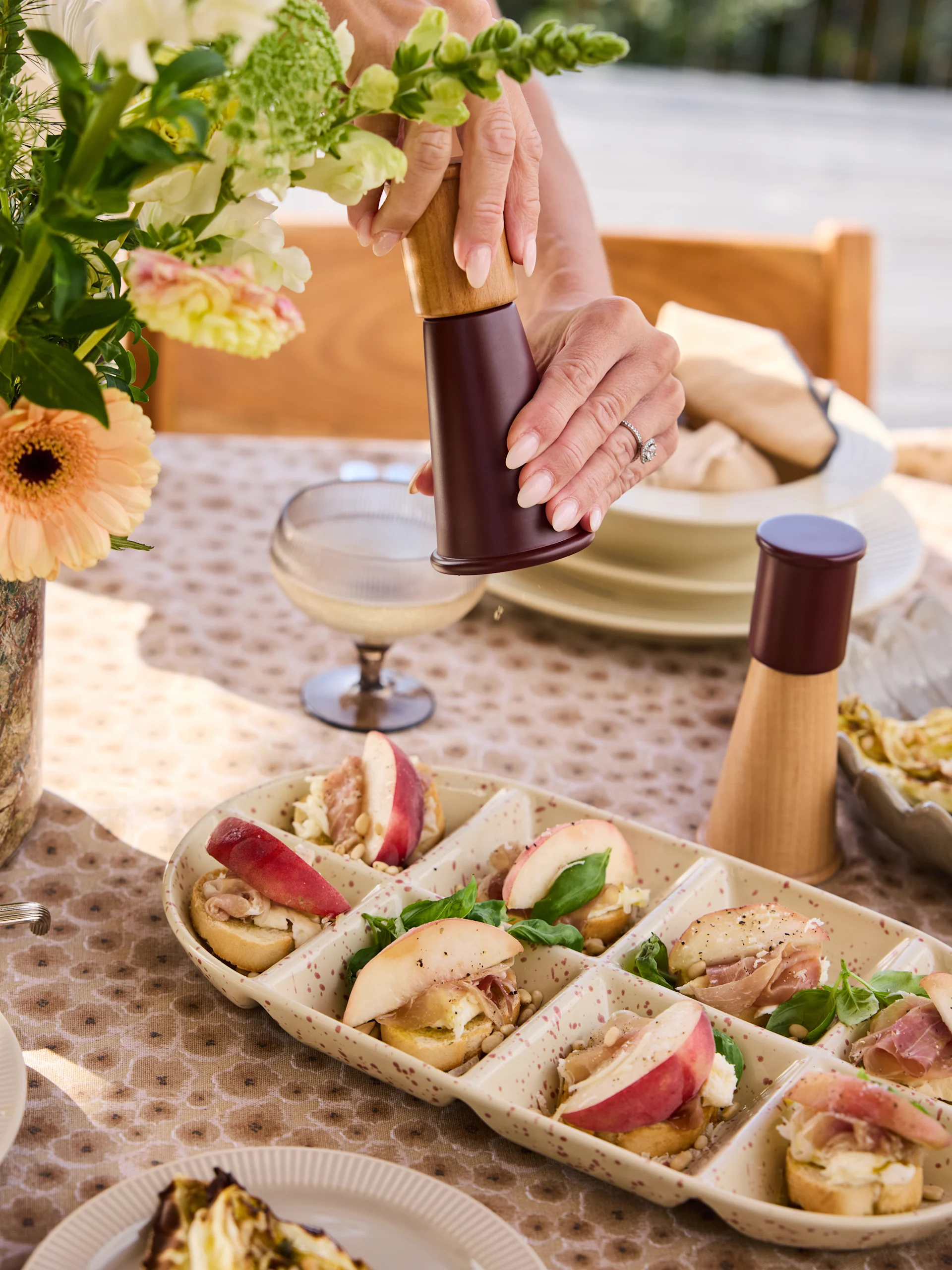 Hænder kværner peber på crostini fad med ferskner, prosciutto, ost, pinjekerner, basilikum.