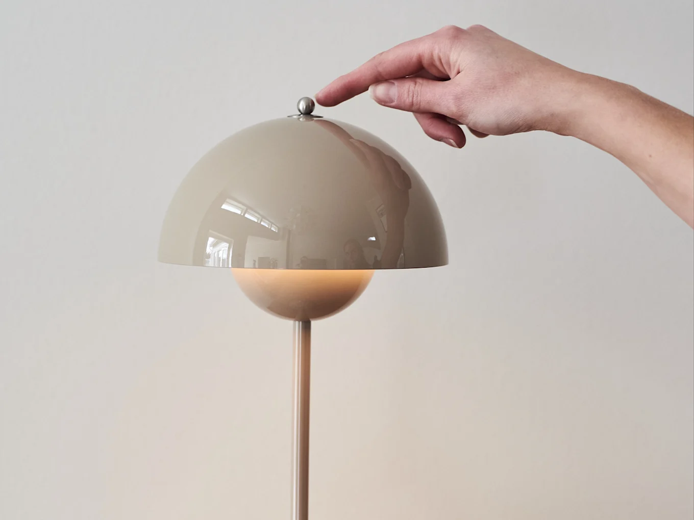 Hånd trykker på en metallisk knap på en beige kuppelformet lampe, der udsender et varmt skær.