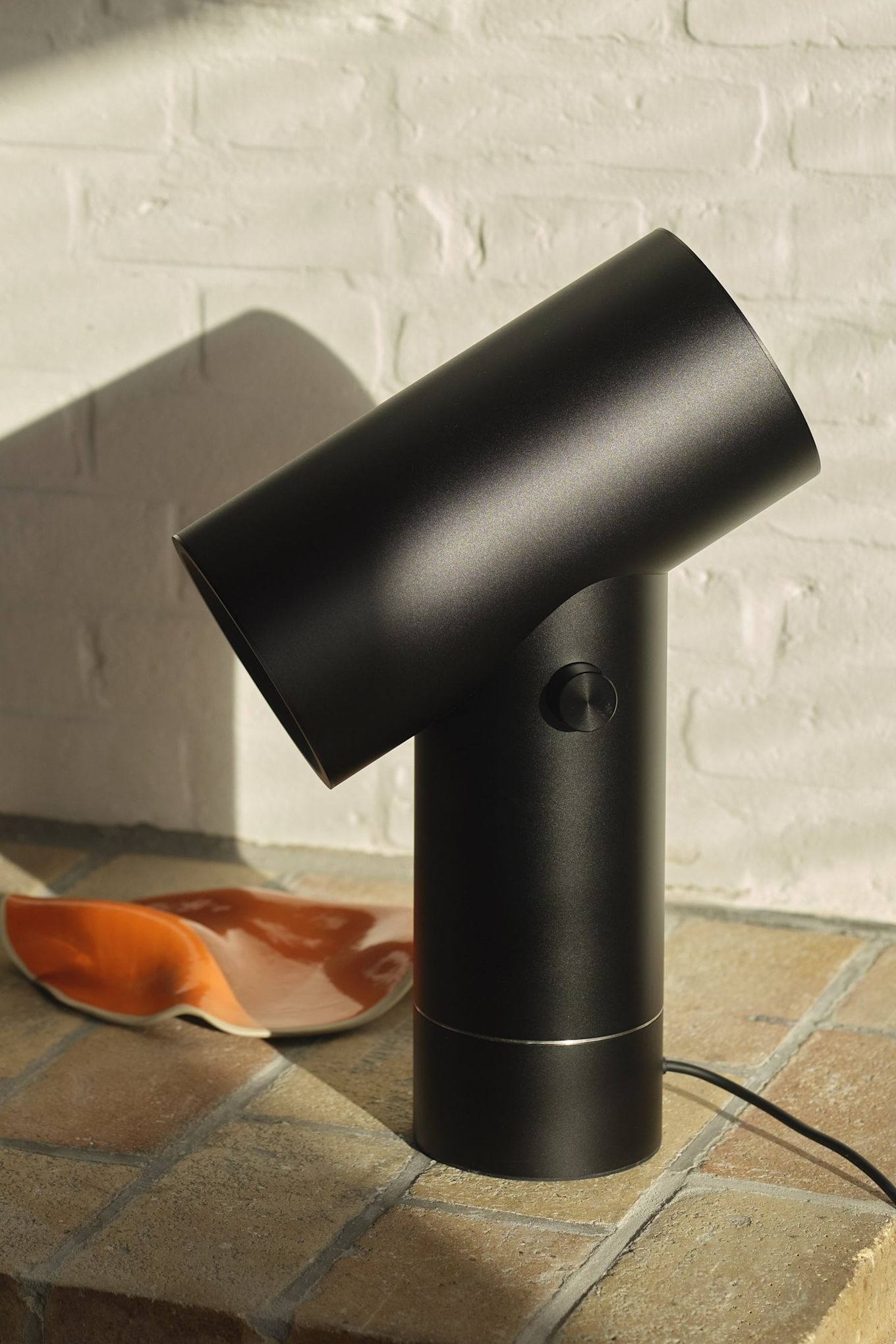 Den sorte bordlampe Beam fra Muuto foran en murvæg.