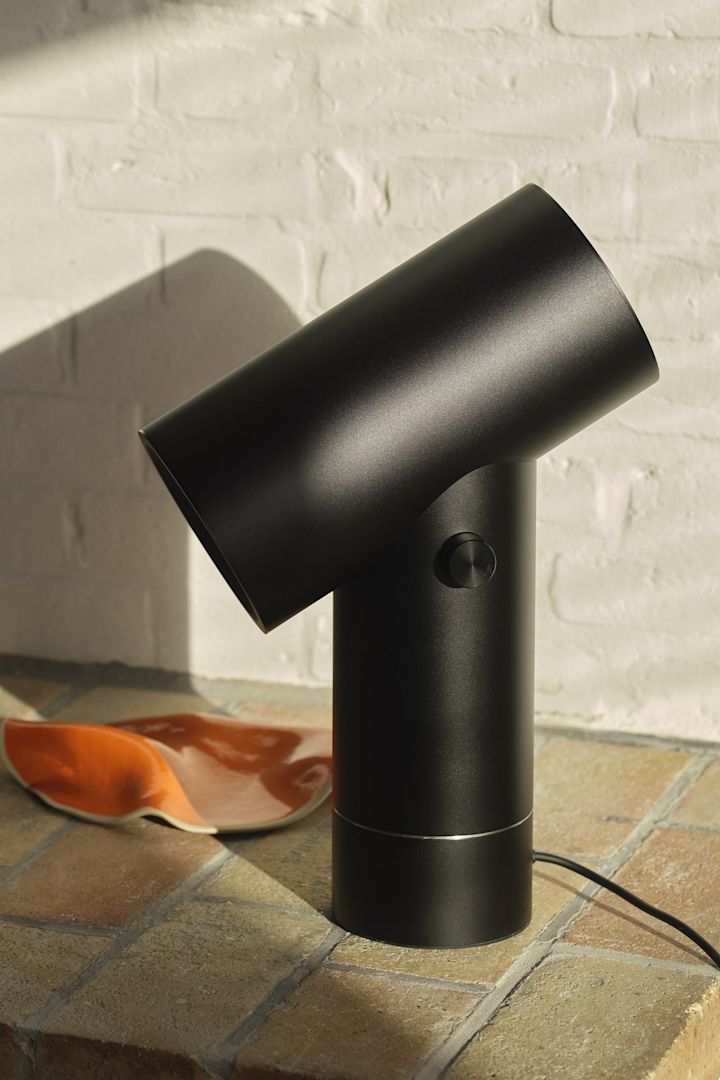 Den sorte bordlampe Beam fra Muuto foran en murvæg.