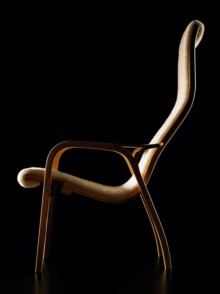 En elegant loungestol med buet lyst træstel og creme pelsbetræk, mod en sort baggrund.