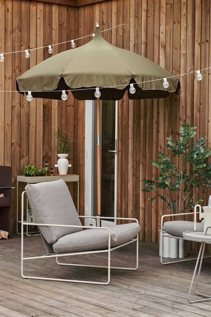 En hyggelig træ terrasse med lyskæder, parasollen Lull og lænestolen Desert, begge fra Ferm Living.