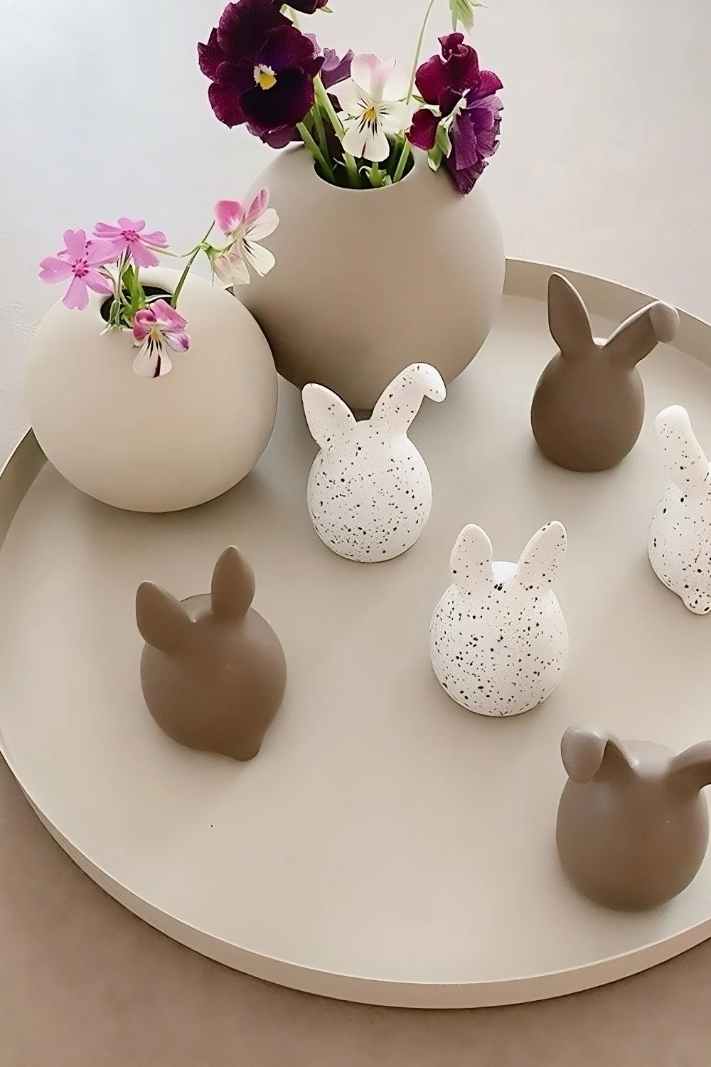 Trillinger af tofarvede påskeharer fra DBKD står på en bakke ved siden af to kuglevaser fra Cooee Design i @sachi_roooms hjem.