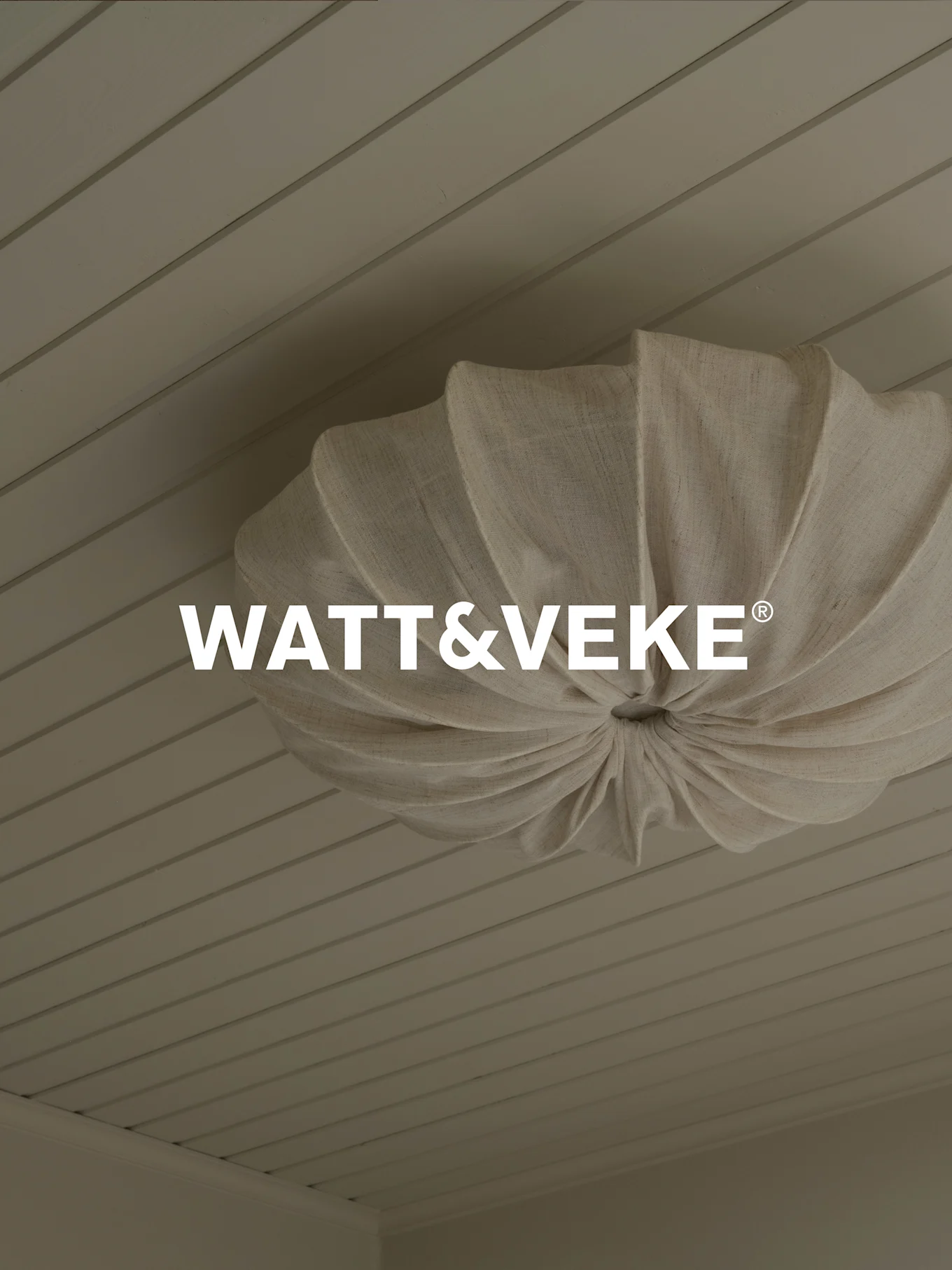 WATT&VEKE® logo over en plisseret loftslampe i naturligt stof på et lyst træloft.
