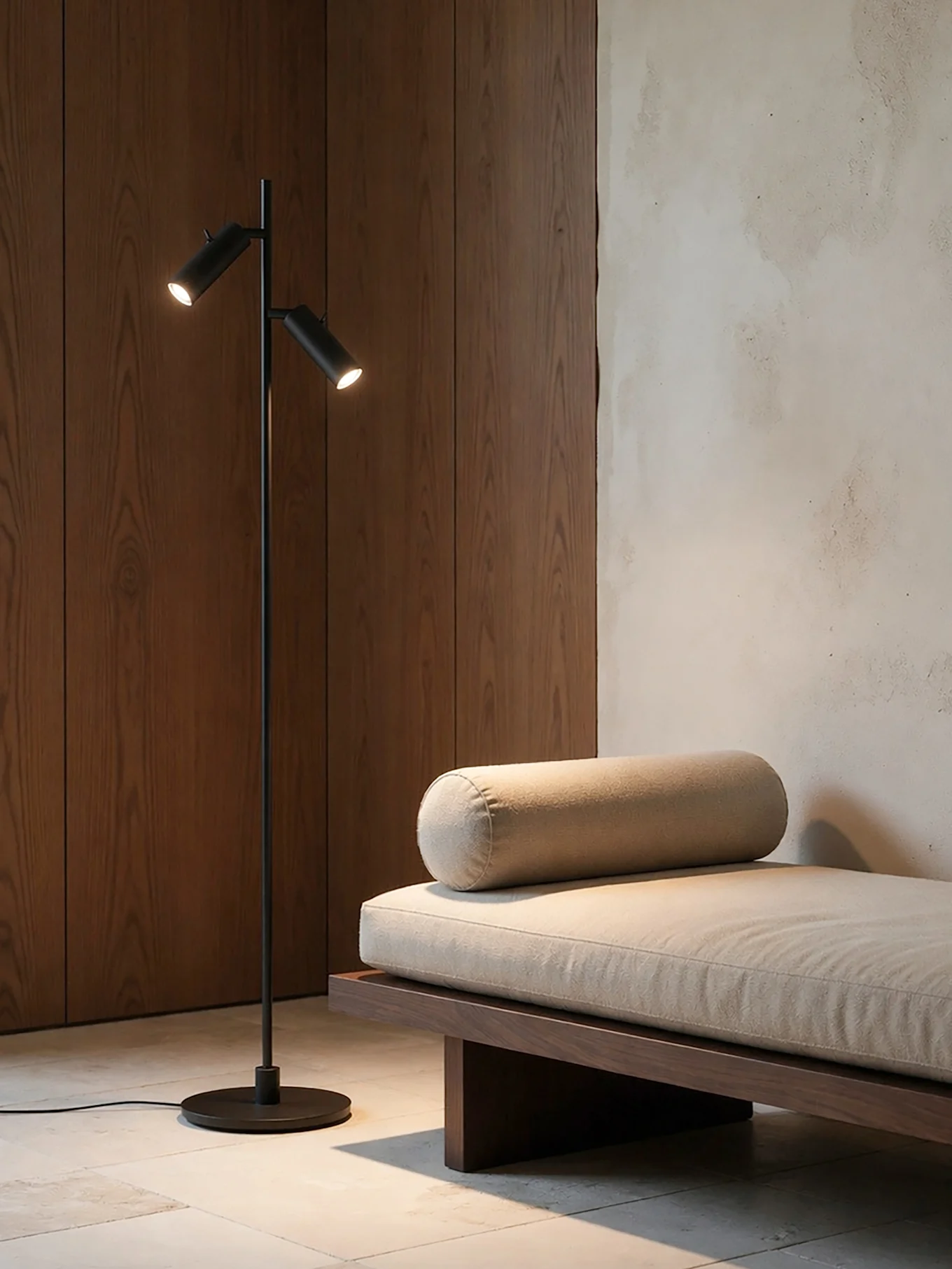 Et moderne rum med en sort gulvlampe med to lys ved siden af en trædaybed med en lys beige hynde og en rullepude.