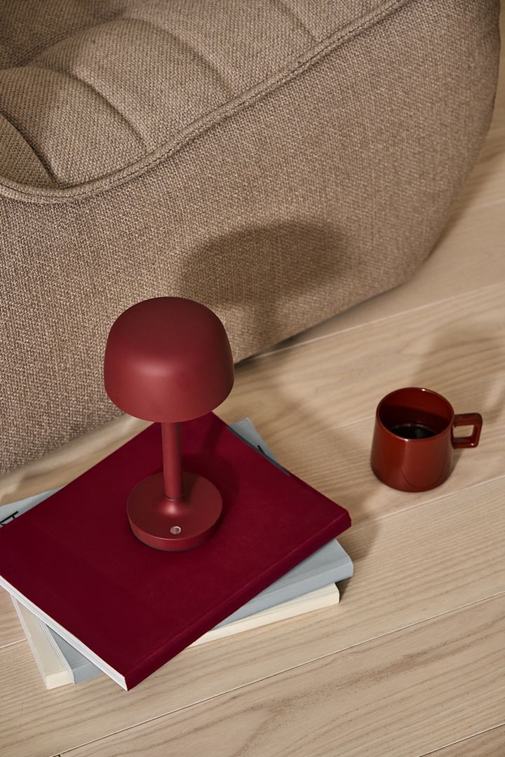 En af efterårets store trends 2024 er krom. Her ser du den klassiske bærbare lampe FlowerPot VP9 i krom fra &Tradition, stående på en skammel ved siden af et glas champagne.