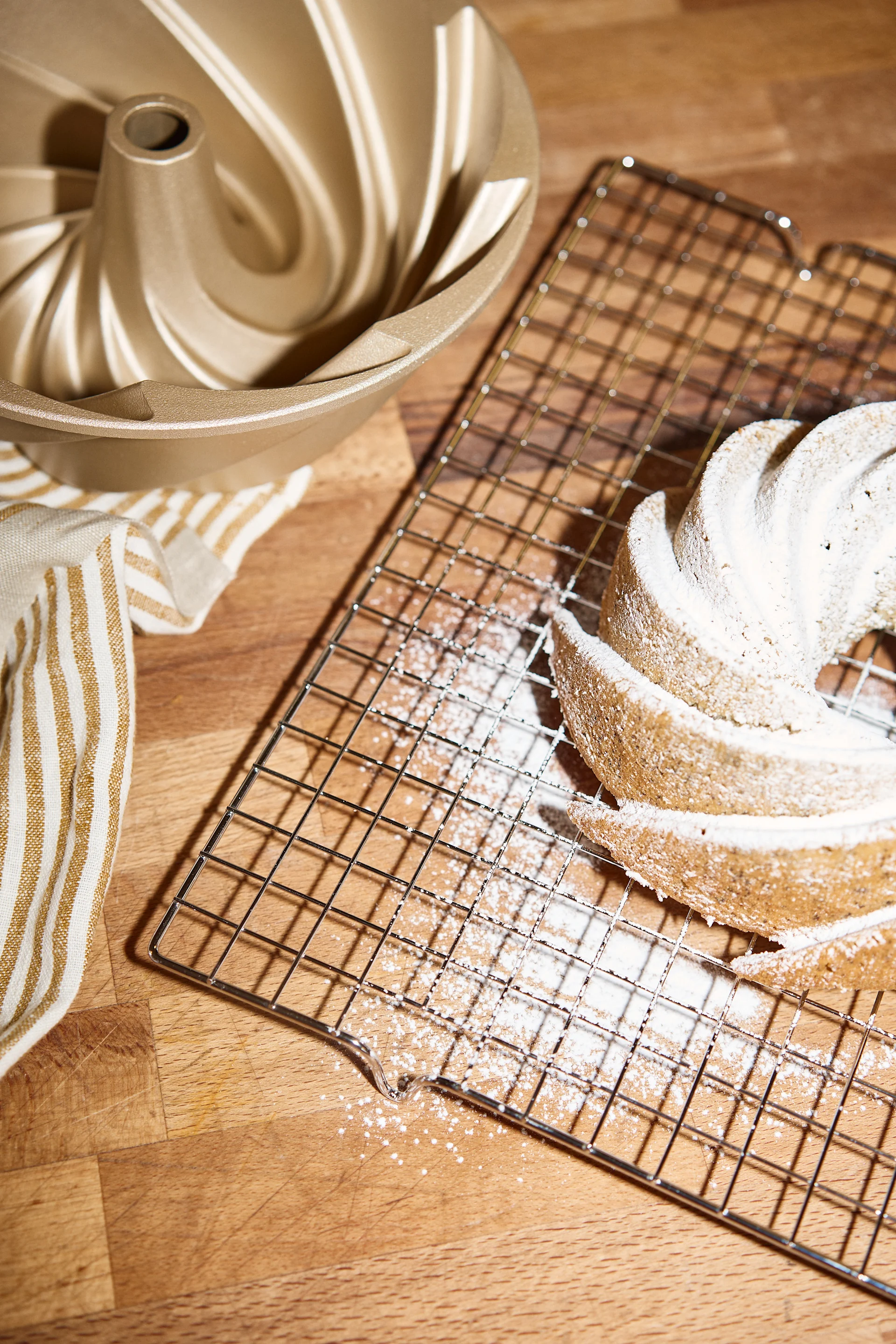 En gylden bundtform, et stribet håndklæde og en bundtkage dækket med flormelis på en bagerist.