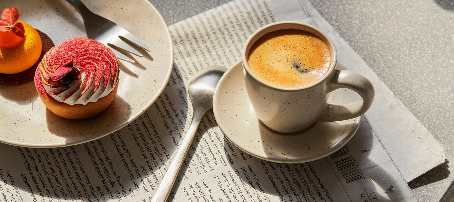 Kaffekop og to kager, en rød tærte og en orange, på en avis.