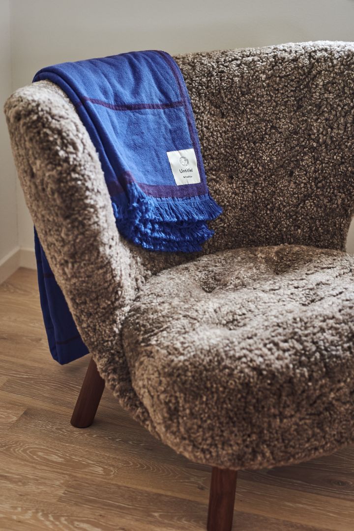 Her ser du Little Petra lænestolen i en pjusket fåreskind variant med det blå Untitled sengetæppe draperet over ryglænet, begge fra &Tradition.