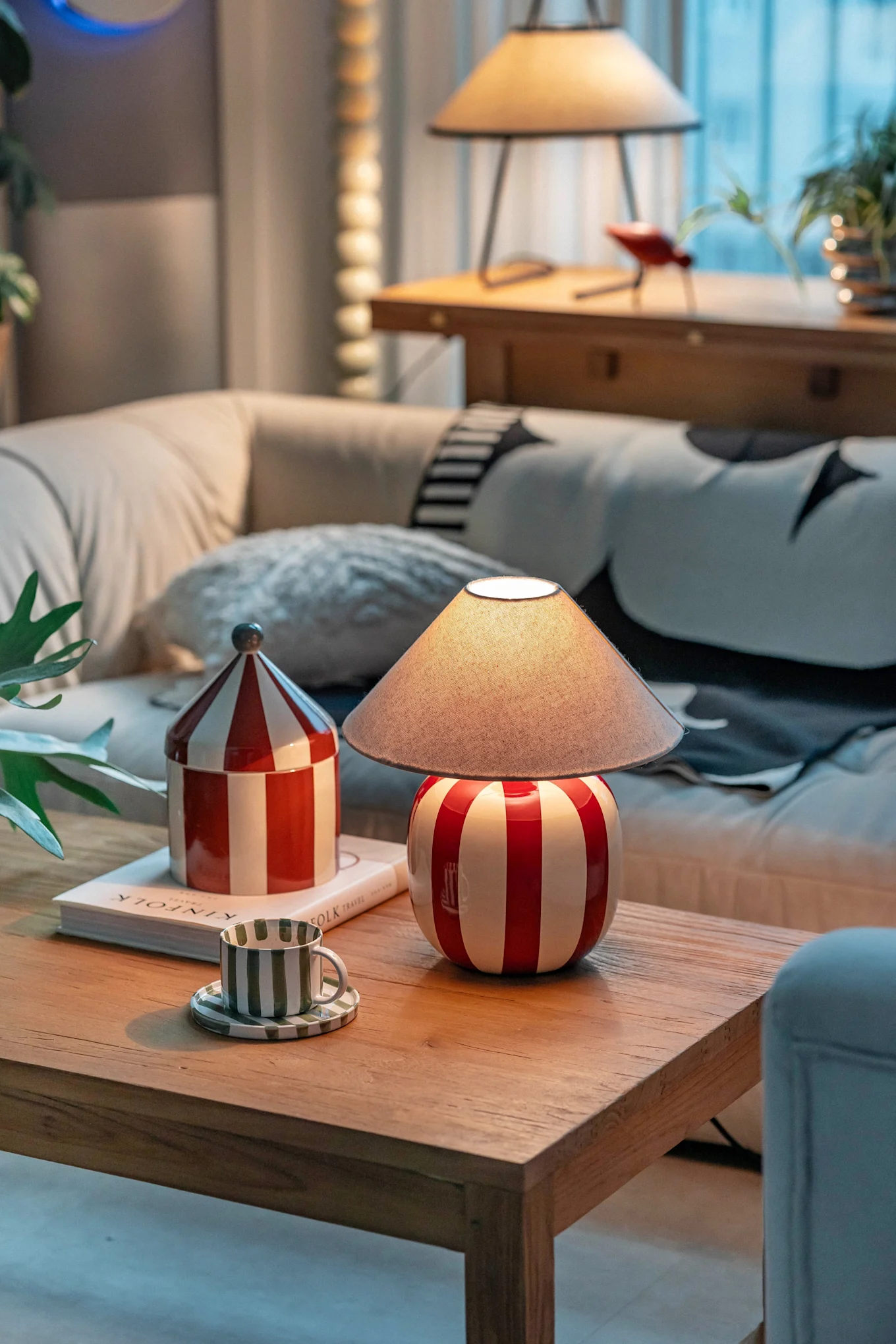 En hyggelig stue med en rød-hvidstribet lampe, matchende beholder og en grønstribet kop på et træ sofabord.