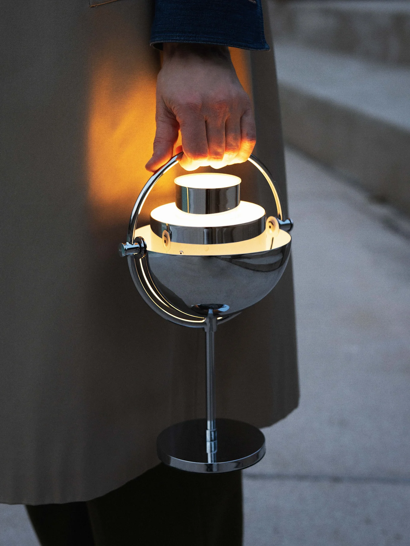 Hånd holder en glødende, moderne bærbar kromlampe.