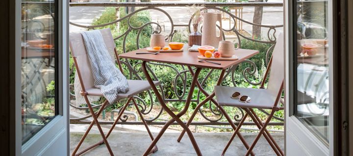 En lille balkon med terrakotta farvet stole og bord der kan foldes.