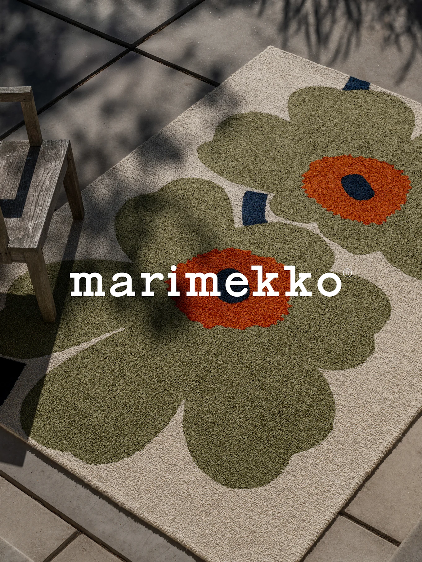 Marimekko tæppe med stort grønt og orange blomstermønster på en terrasse med en træstol.