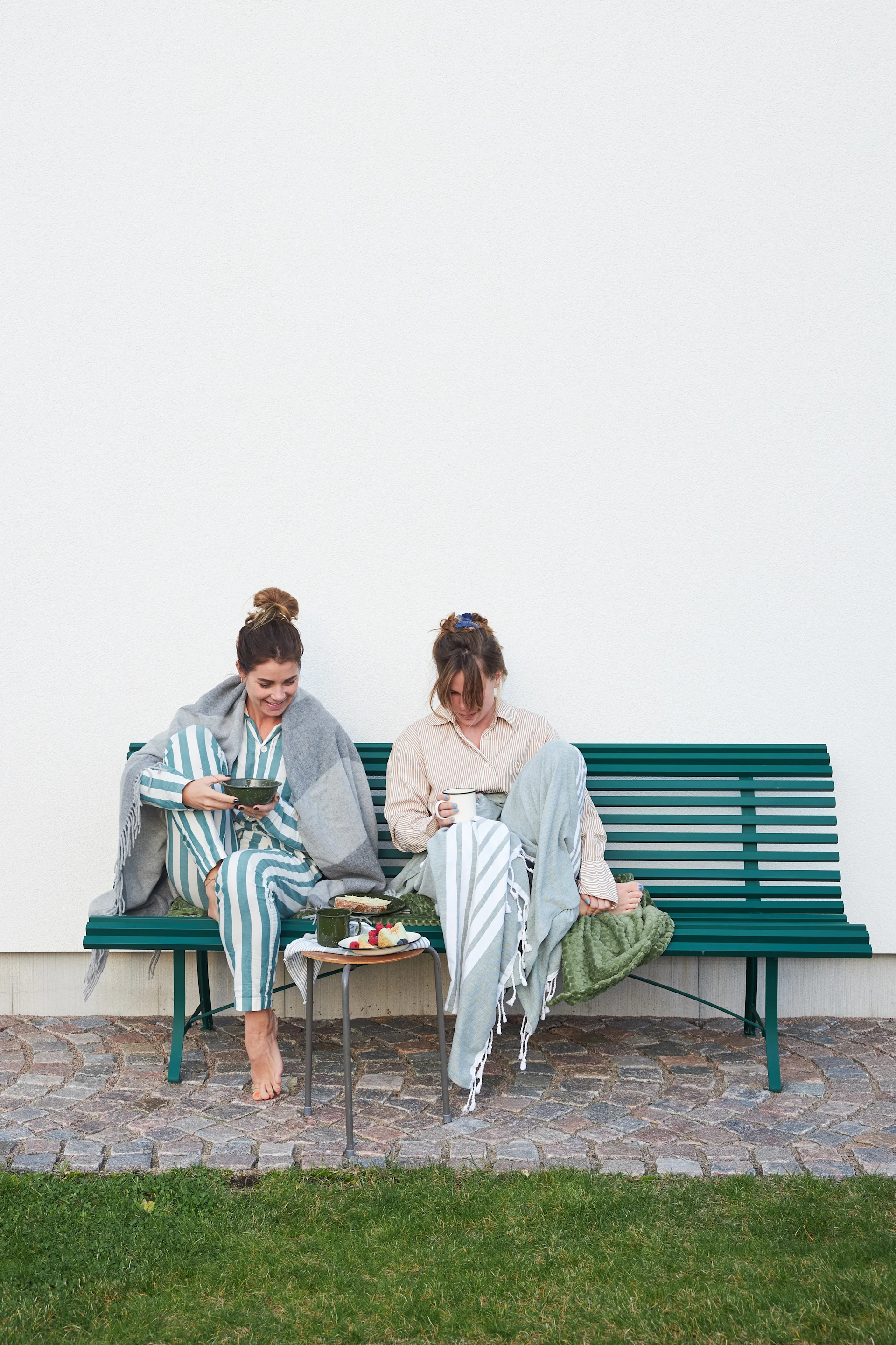 Her ses to kvinder som sidder på en bænk og nyder lidt fika sammen.
